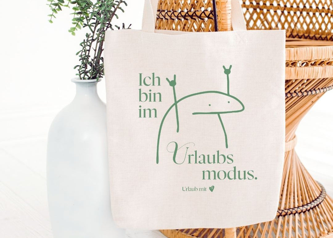 Stofftasche aus Baumwolle mit grünem Aufdruck „Ich bin im Urlaubsmodus“ und lustiger Figur als Willkommensgeschenk für Gäste in einer modernen Ferienwohnung.
